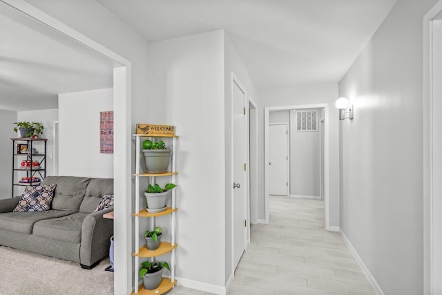 hallway featuring light wood-style floors, visible vents, and baseboards