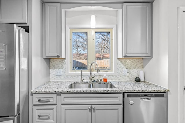 kitchen featuring light stone counters, stainless steel appliances, a sink, and gray cabinetry