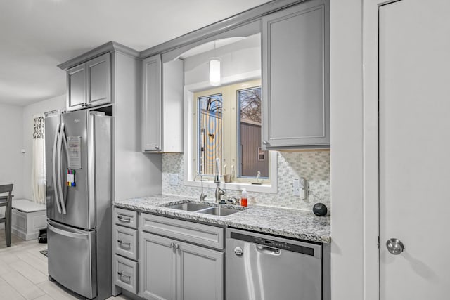 kitchen featuring tasteful backsplash, appliances with stainless steel finishes, light stone counters, and a sink