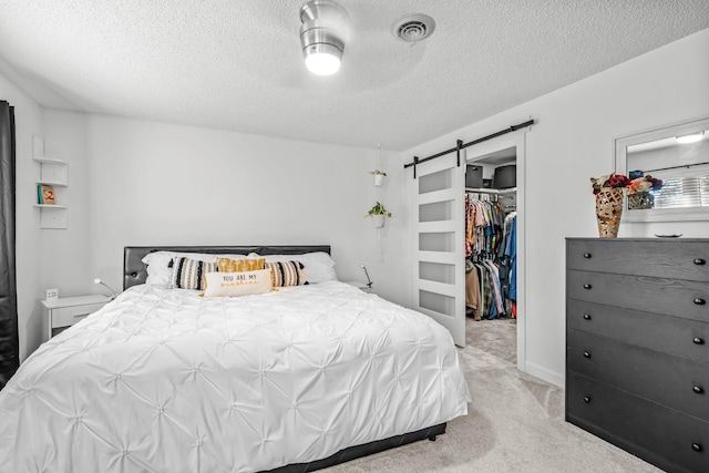 bedroom with a barn door, light carpet, visible vents, a spacious closet, and a closet