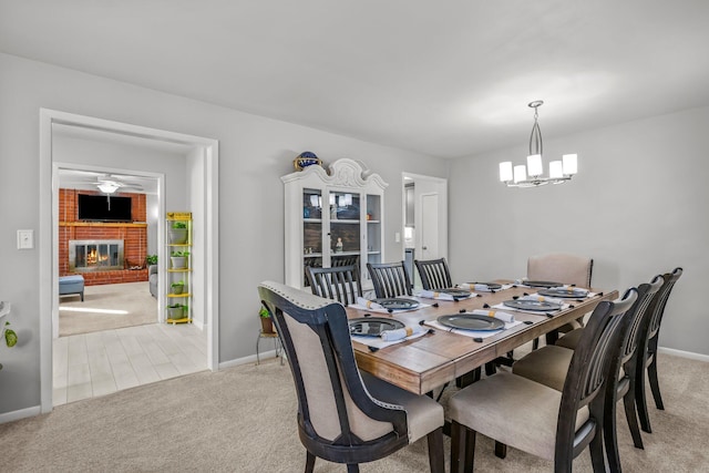 dining room featuring light carpet, a fireplace, a notable chandelier, and baseboards