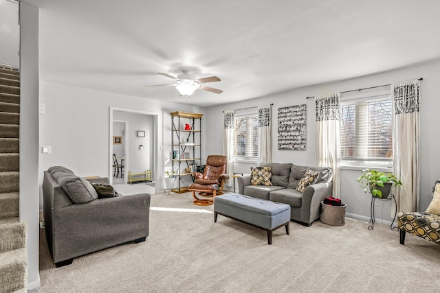 living room featuring stairs, ceiling fan, baseboards, and light colored carpet