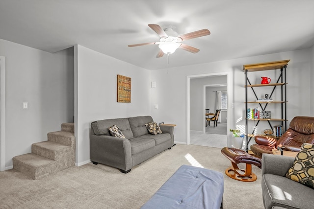 living room with a ceiling fan, light colored carpet, stairway, and baseboards