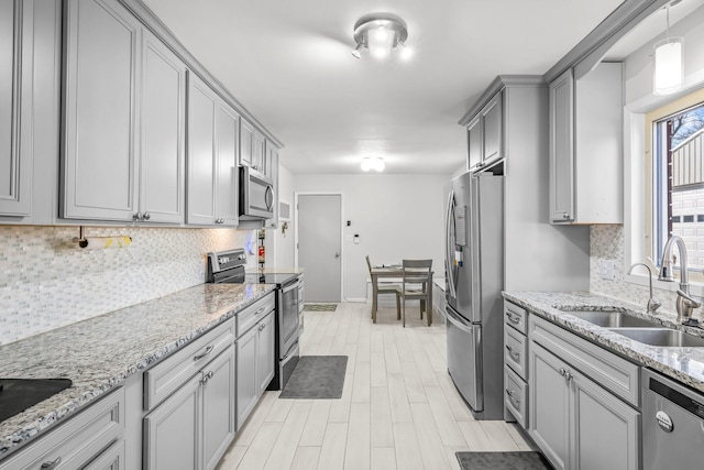 kitchen with stainless steel appliances, backsplash, a sink, and light stone countertops