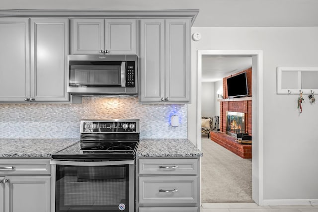 kitchen with light stone counters, a fireplace, light colored carpet, backsplash, and appliances with stainless steel finishes