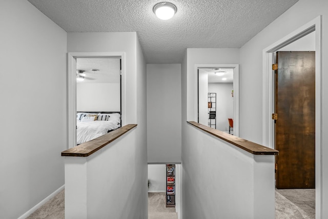 hallway with baseboards, light colored carpet, a textured ceiling, and an upstairs landing