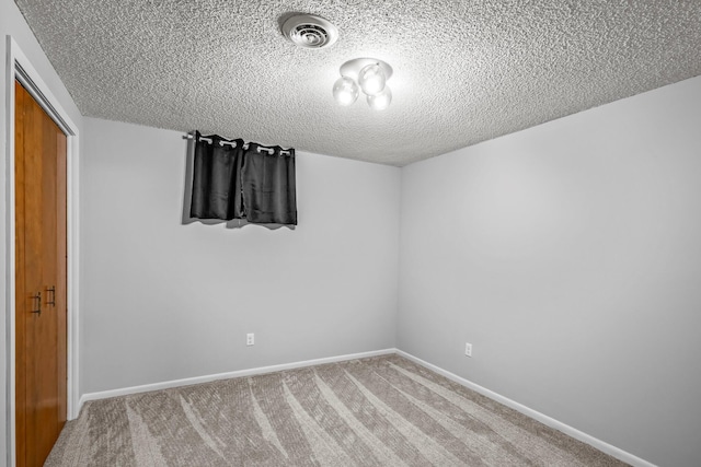 unfurnished room featuring a textured ceiling, carpet flooring, visible vents, and baseboards