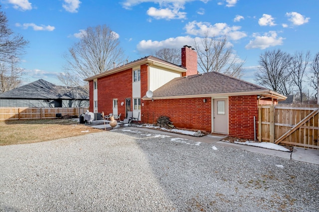 view of home's exterior with brick siding, fence, driveway, roof with shingles, and a chimney