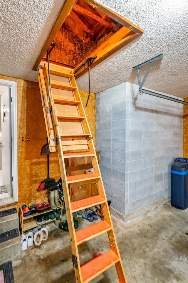 stairway featuring a textured ceiling, concrete floors, and concrete block wall