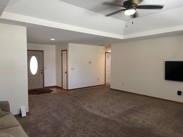 unfurnished living room with ceiling fan, dark colored carpet, a raised ceiling, and baseboards