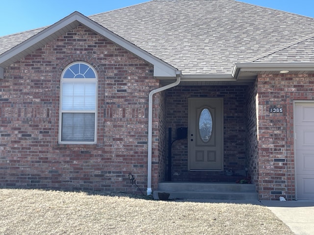 entrance to property featuring a garage, brick siding, and a shingled roof