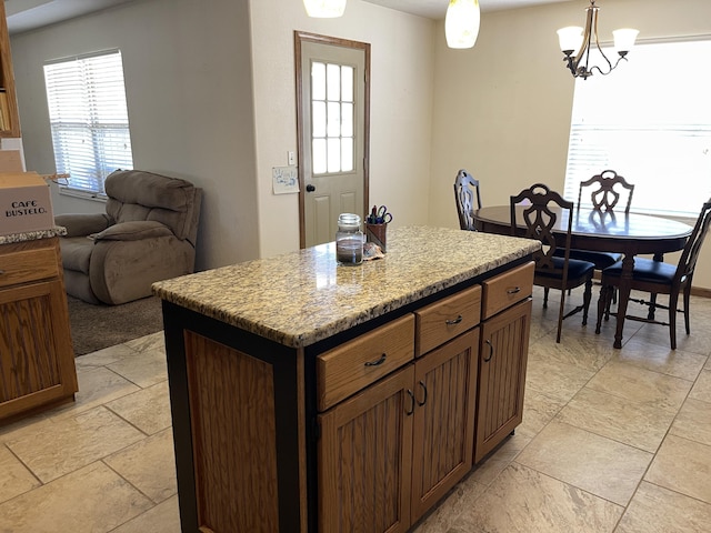 kitchen with hanging light fixtures, a kitchen island, a chandelier, and light stone counters