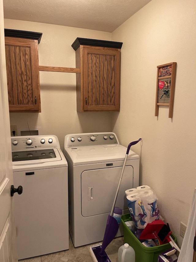 clothes washing area featuring a textured ceiling, washing machine and dryer, and cabinet space