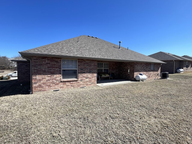 rear view of house featuring brick siding, roof with shingles, and a patio