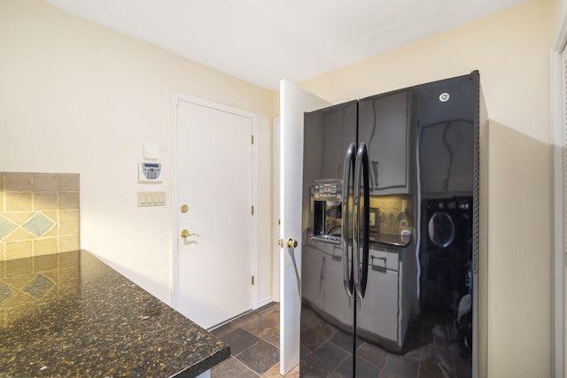 kitchen featuring dark countertops, stone finish floor, black fridge with ice dispenser, and backsplash