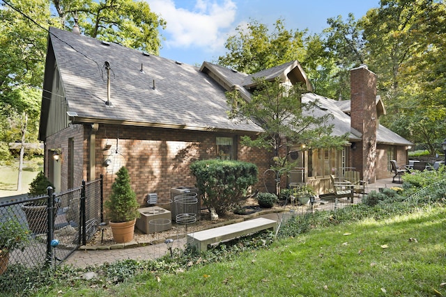 rear view of house featuring brick siding, a shingled roof, fence, a chimney, and a patio area