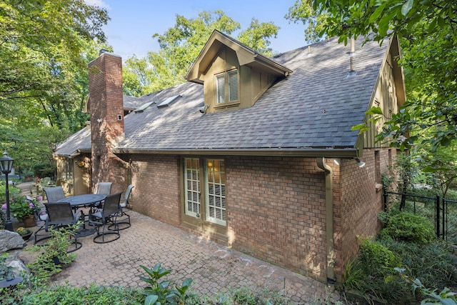 rear view of house with a patio area, fence, brick siding, and roof with shingles