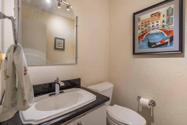 bathroom with a textured wall, vanity, and toilet