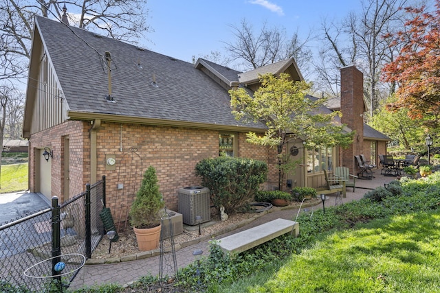 back of house featuring fence, brick siding, roof with shingles, and central air condition unit