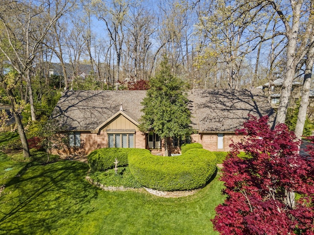 exterior space featuring brick siding, a shingled roof, and a front yard
