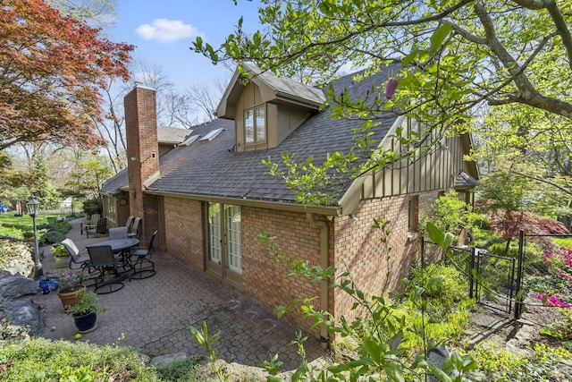 view of side of property featuring roof with shingles, a gate, a chimney, brick siding, and a patio area