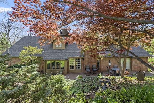 rear view of house featuring brick siding, roof with shingles, and a patio area