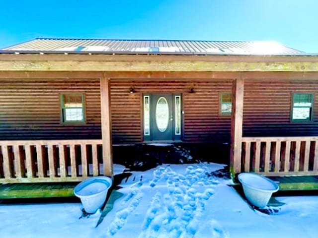 snow covered property entrance featuring covered porch and metal roof