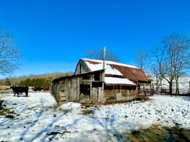 view of snowy exterior with a barn, fence, and an outbuilding