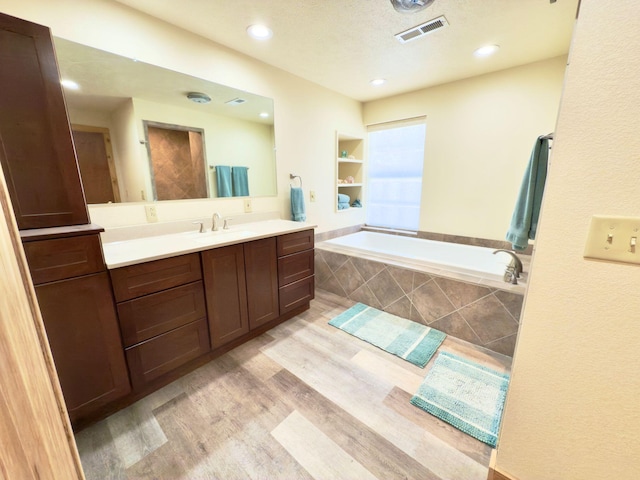 full bath with visible vents, vanity, a textured ceiling, wood finished floors, and a bath