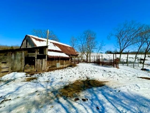 snowy yard featuring a barn, fence, and an outdoor structure