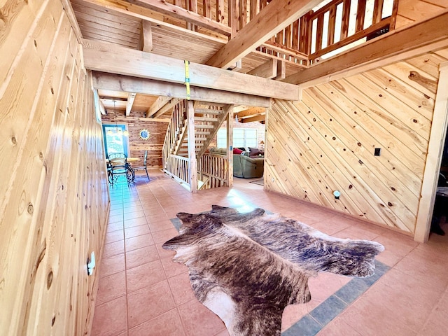 interior space featuring tile patterned flooring, beam ceiling, wood walls, and stairs