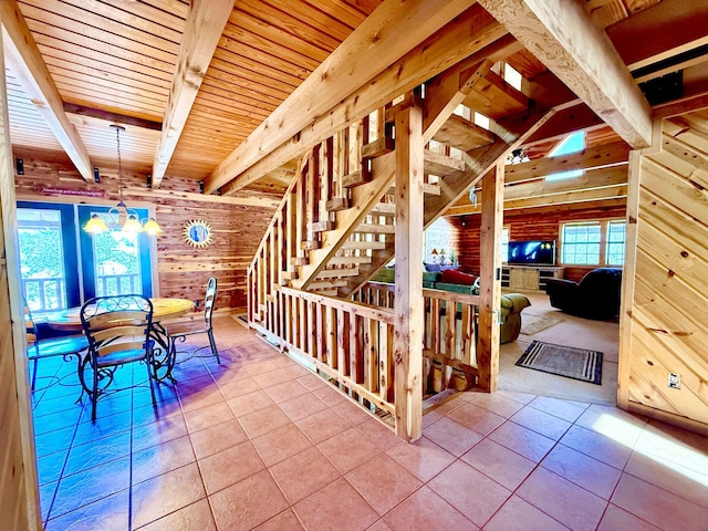 interior space with a chandelier, tile patterned flooring, wood walls, wood ceiling, and beam ceiling