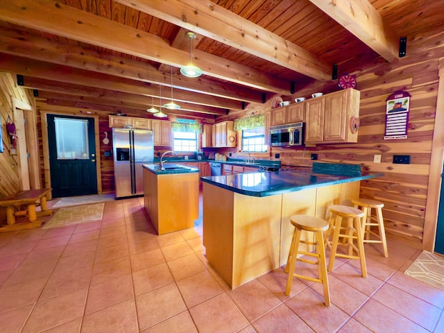 kitchen with a center island, dark countertops, appliances with stainless steel finishes, wood walls, and a sink