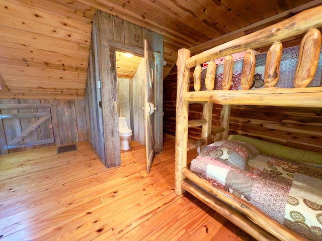 bedroom with wood walls, visible vents, wood ceiling, light wood-type flooring, and ensuite bath