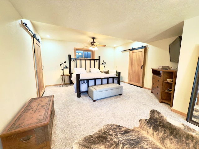 bedroom featuring a textured ceiling, a barn door, baseboards, and light colored carpet