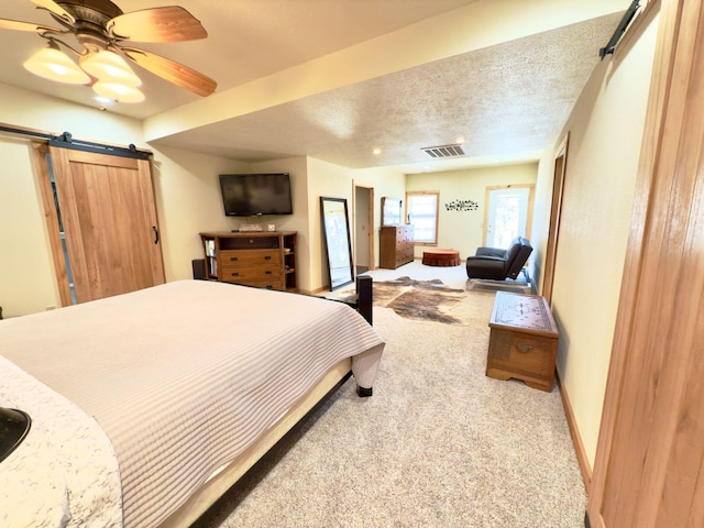 bedroom featuring light carpet, a barn door, baseboards, visible vents, and a textured ceiling