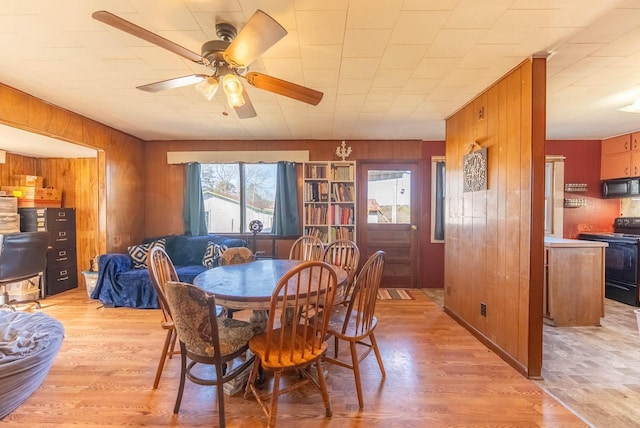 dining space featuring light wood-type flooring, a ceiling fan, and wooden walls