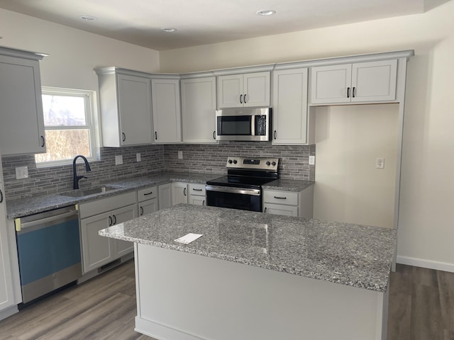 kitchen with wood finished floors, stainless steel appliances, light stone counters, and a sink