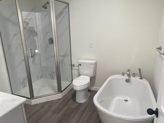 bathroom featuring a marble finish shower, a freestanding bath, toilet, wood finished floors, and baseboards