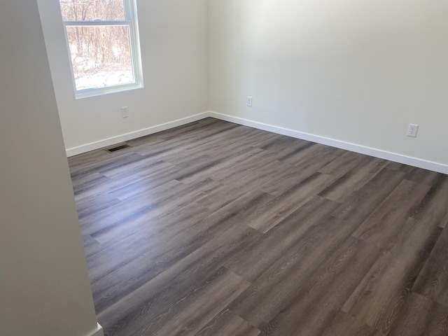 spare room featuring dark wood-style floors, visible vents, and baseboards