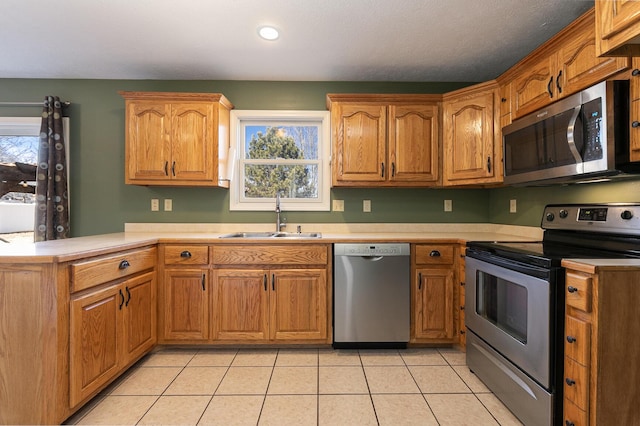 kitchen featuring light tile patterned floors, appliances with stainless steel finishes, a peninsula, light countertops, and a sink