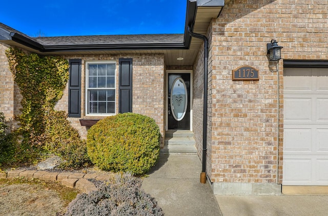 entrance to property with a garage, brick siding, and a shingled roof