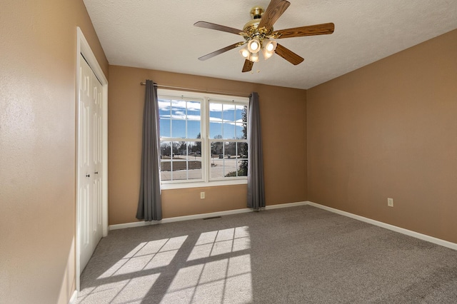 spare room featuring a textured ceiling, carpet floors, ceiling fan, and baseboards