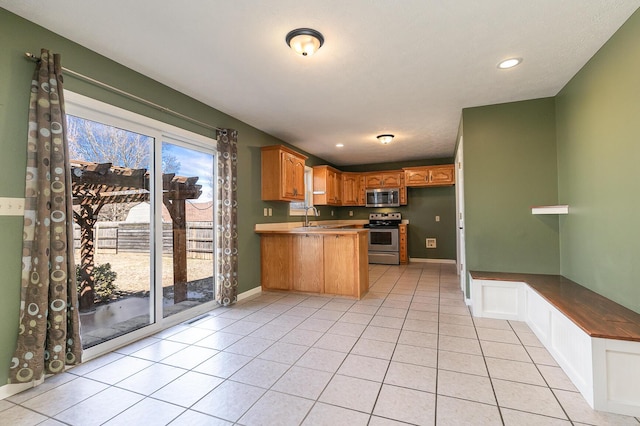 kitchen featuring light tile patterned floors, appliances with stainless steel finishes, a sink, a peninsula, and baseboards