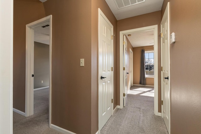 hallway with light carpet, visible vents, and baseboards