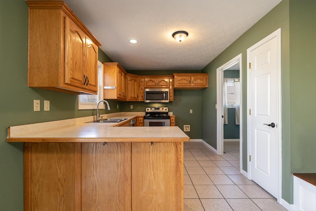 kitchen featuring light tile patterned floors, stainless steel appliances, a peninsula, a sink, and brown cabinets