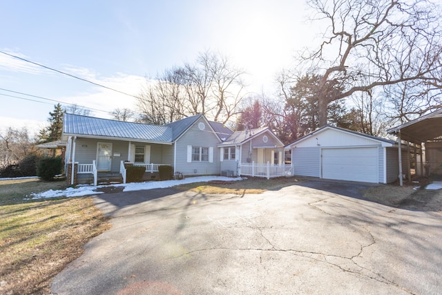 single story home with an outbuilding, a detached garage, a porch, metal roof, and driveway