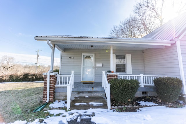 snow covered property entrance featuring covered porch and metal roof