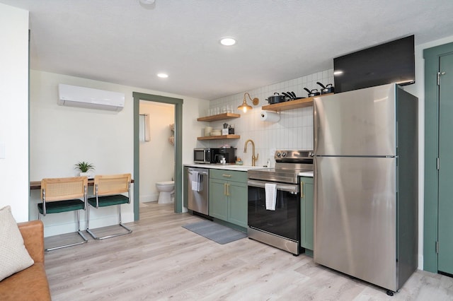 kitchen featuring appliances with stainless steel finishes, light wood-style floors, green cabinets, a sink, and a wall mounted AC