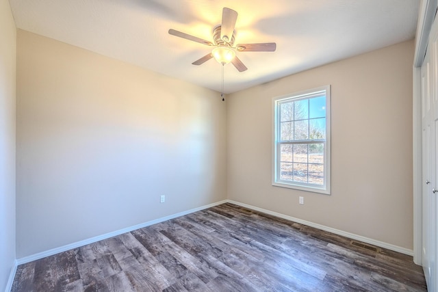 spare room with dark wood-style floors, visible vents, ceiling fan, and baseboards